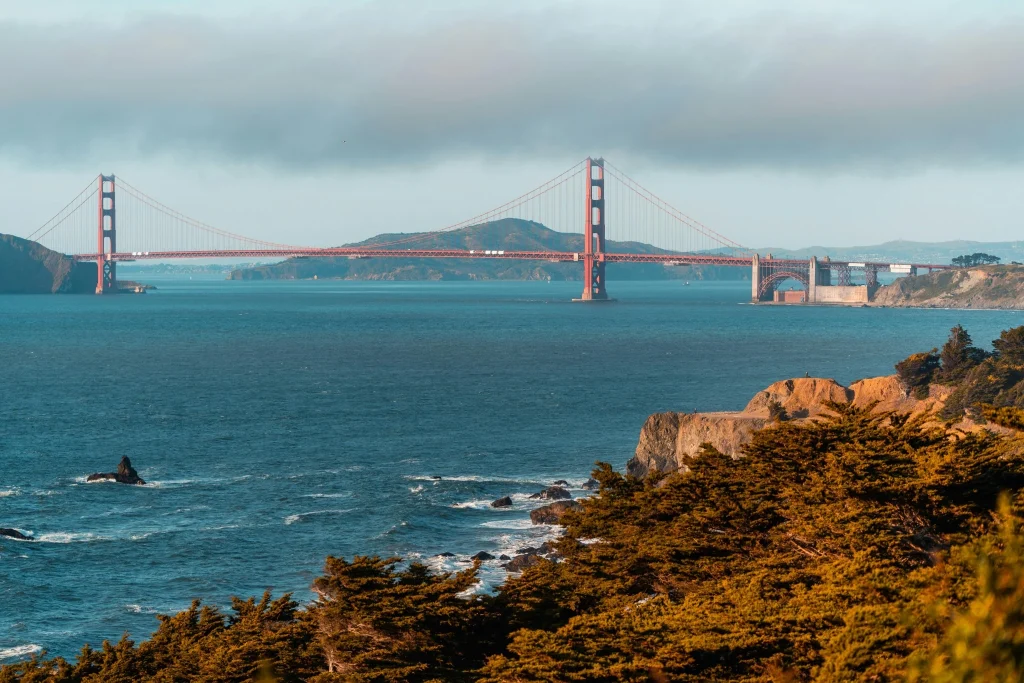 Scenic view of the Golden Gate Bridge in San Francisco with ocean waters, coastal cliffs, and cloudy skies during daytime.