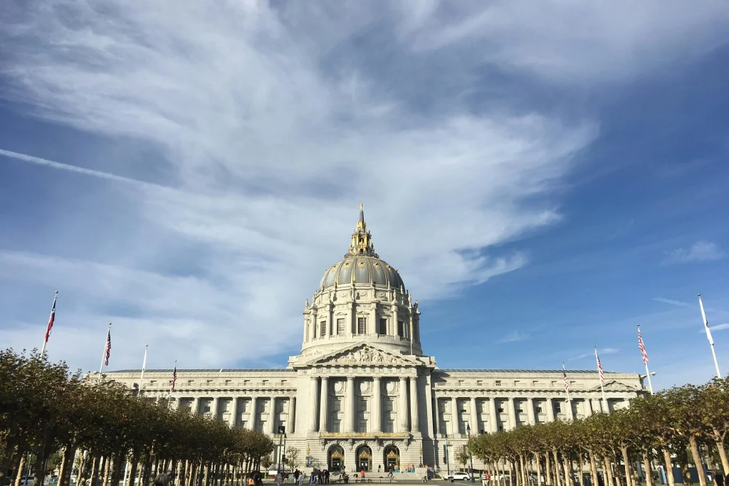 Front view of San Francisco City Hall with its iconic dome architecture and dramatic cloudy blue sky.