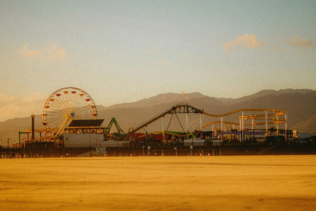 View of Santa Monica Pier featuring a Ferris wheel, roller coaster, and beach during golden hour in California.